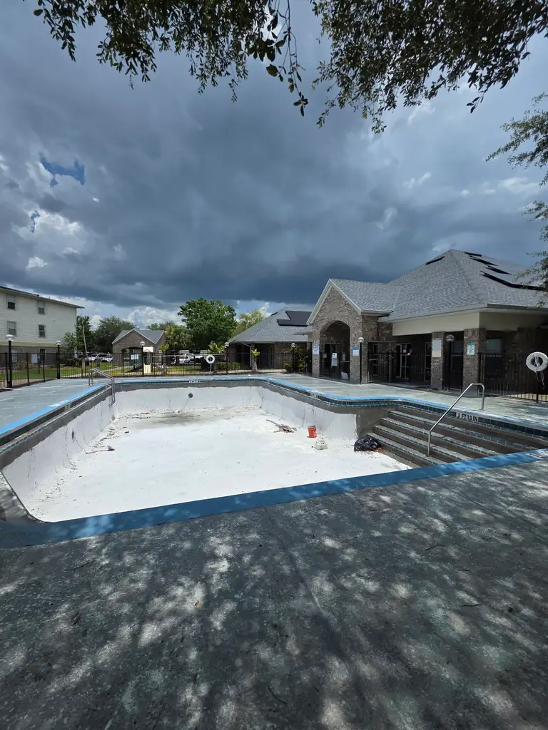 Drained community swimming pool with a worn gray deck before surface restoration.