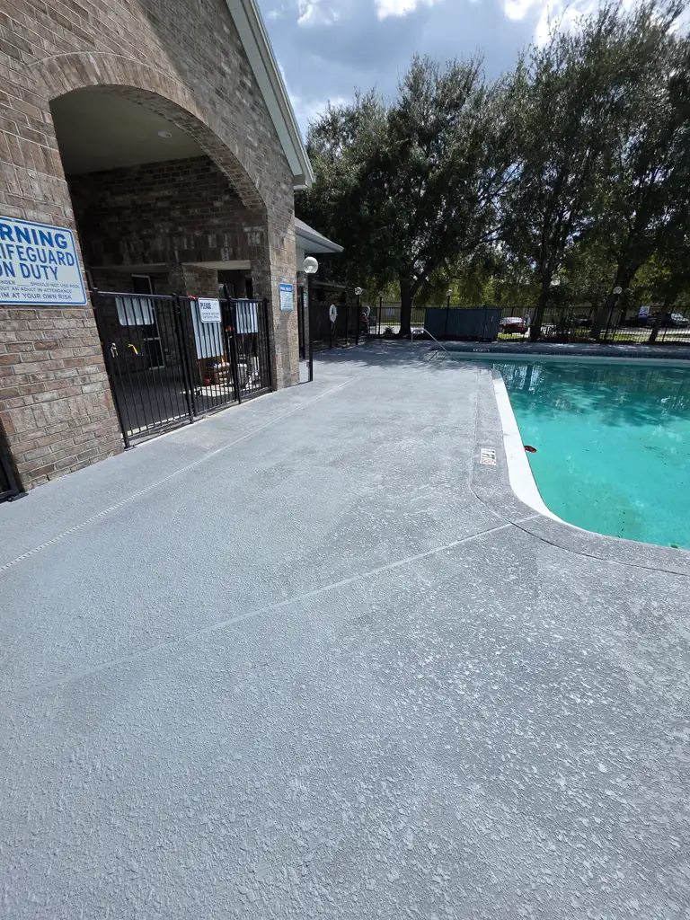 Refilled community swimming pool beside a continuous finished gray deck after surface restoration.
