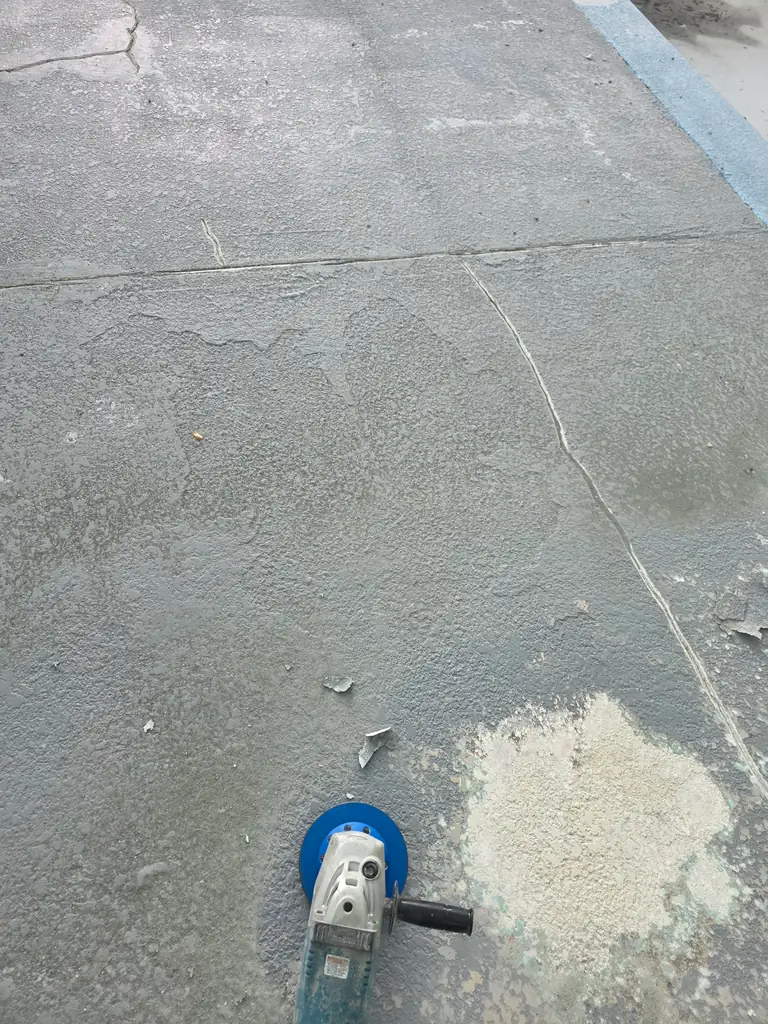 Hand grinder beside an opened section of deteriorated coating on a community pool deck.