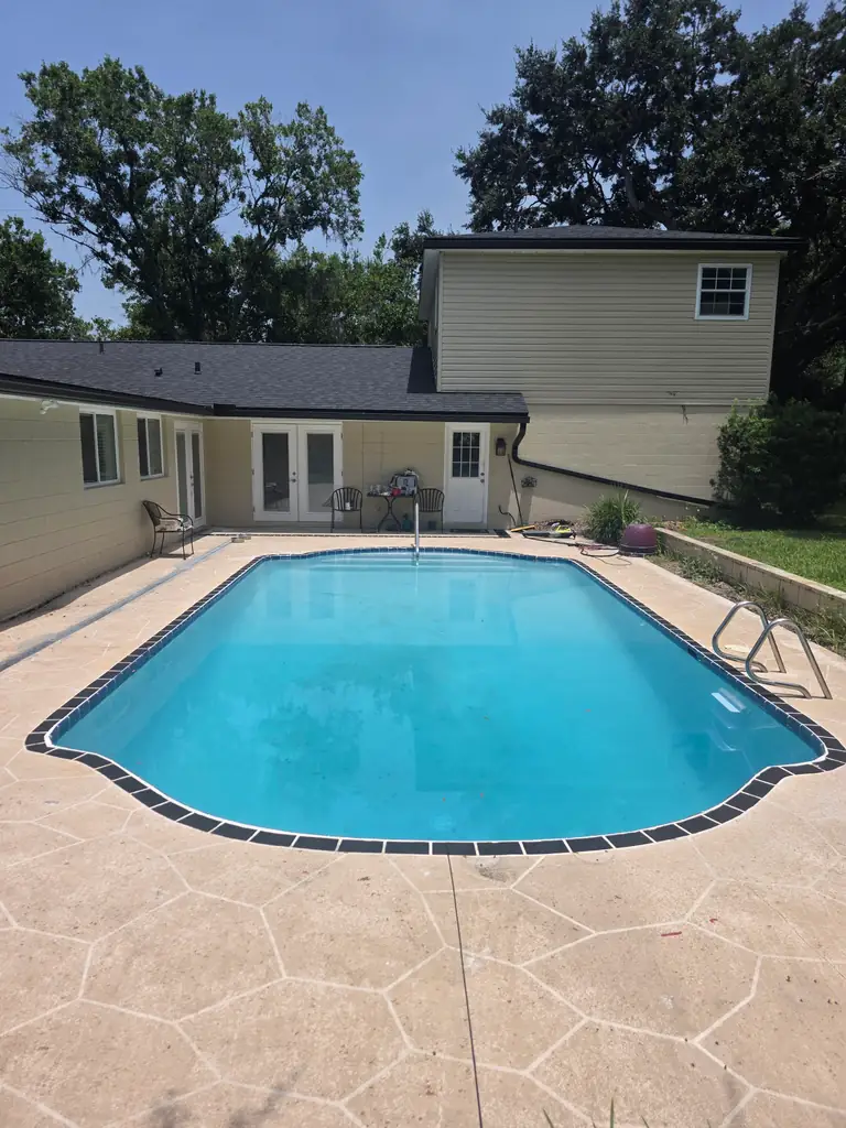 Wide later view of the refilled residential pool with tools and hoses around the work area.