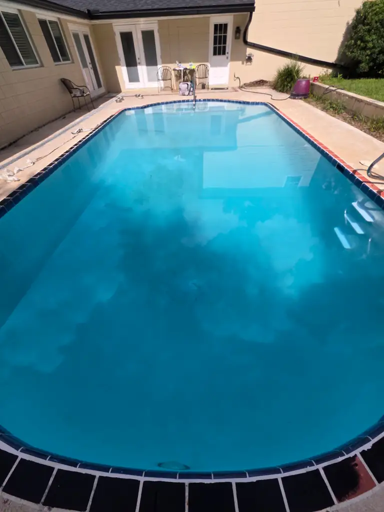 Close view of the refilled residential pool and lighter interior beneath blue water, with closeout materials on the deck.