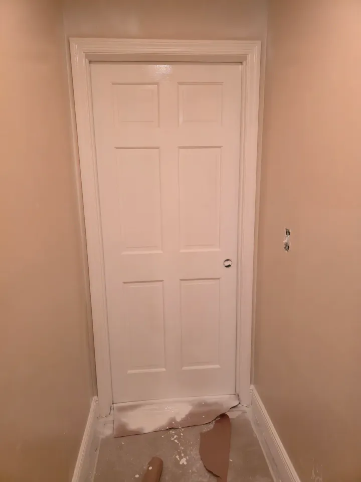 White interior door and trim during active coating work, with floor protection and unfinished hardware details visible.