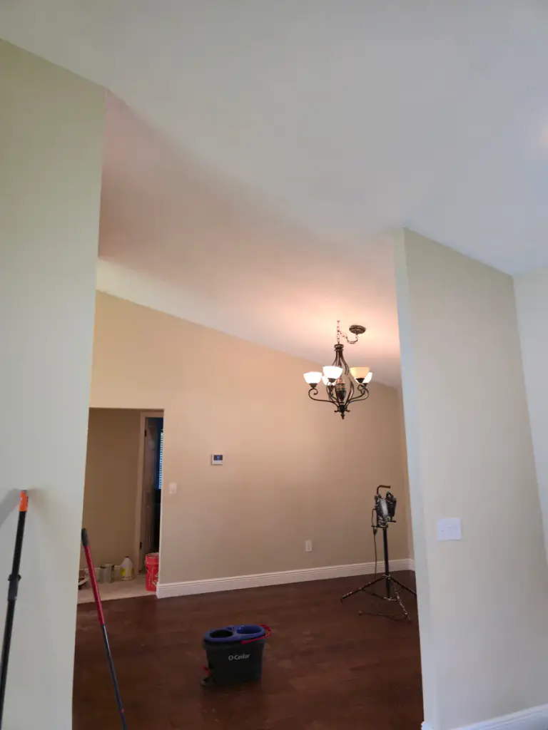 Interior room during repainting with beige walls, white ceiling and trim, and work equipment visible.
