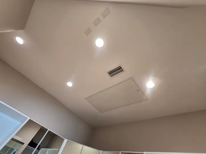 White interior ceiling with recessed lights and an access panel above a storage area