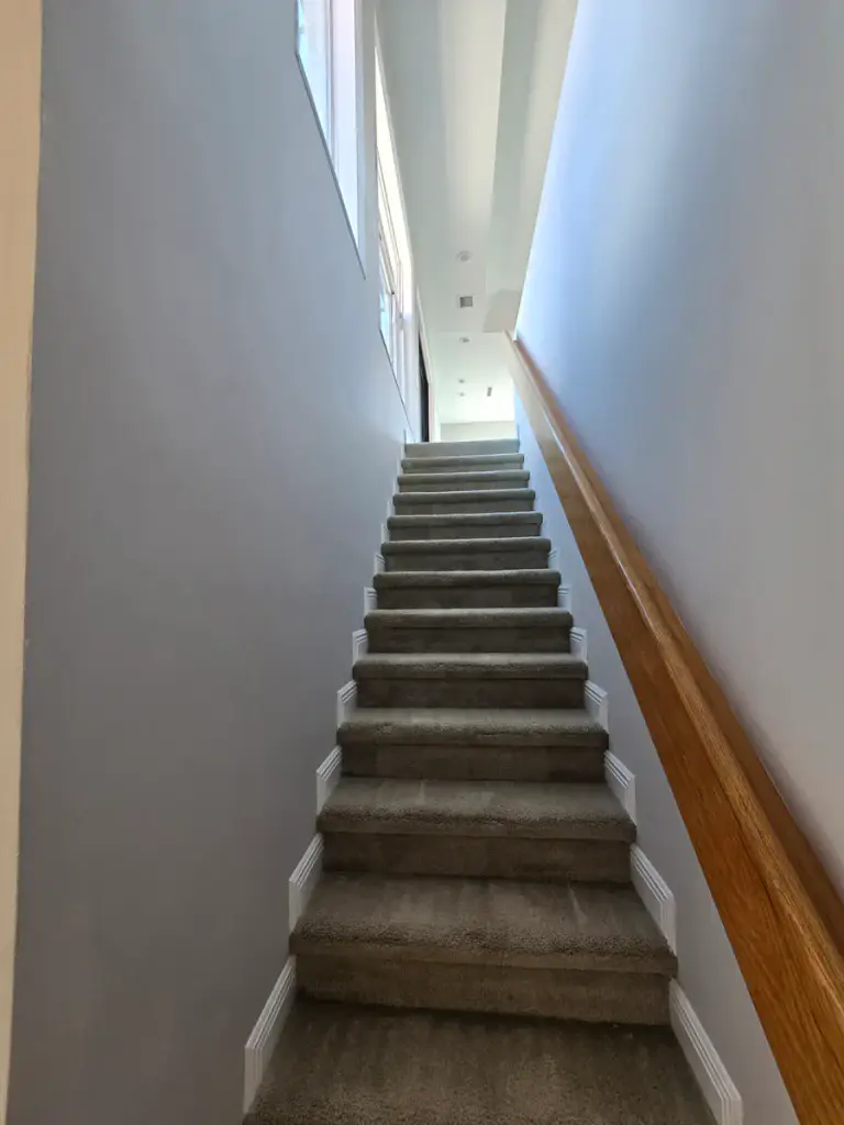 Interior stairwell with finished gray walls, white base trim, and a wood handrail