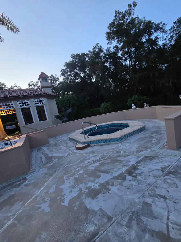 Mottled pool-deck surface during preparation around a residential pool courtyard.