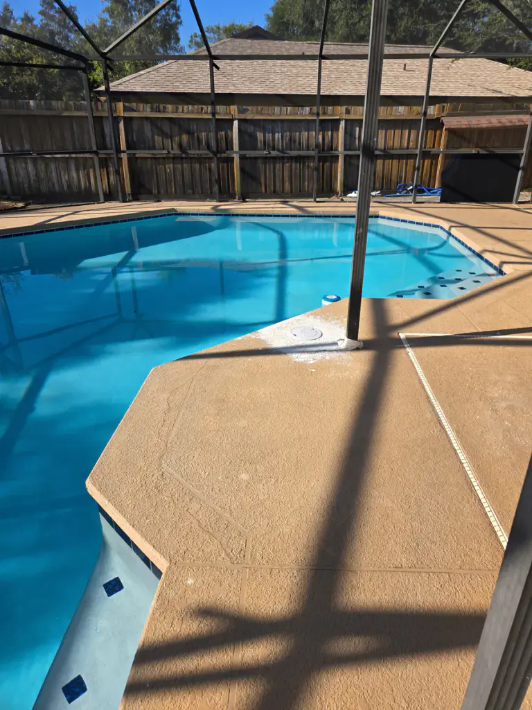 Light neutral coated deck following the curved edge of a screened residential pool.
