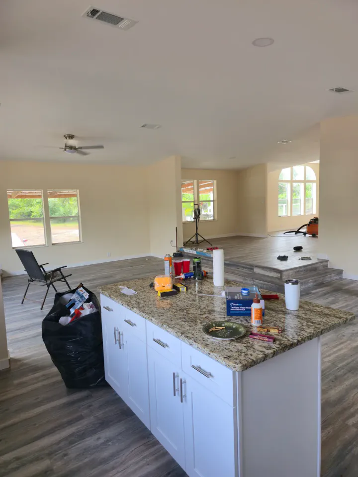 Kitchen and open living area with installed flooring and work materials still present.